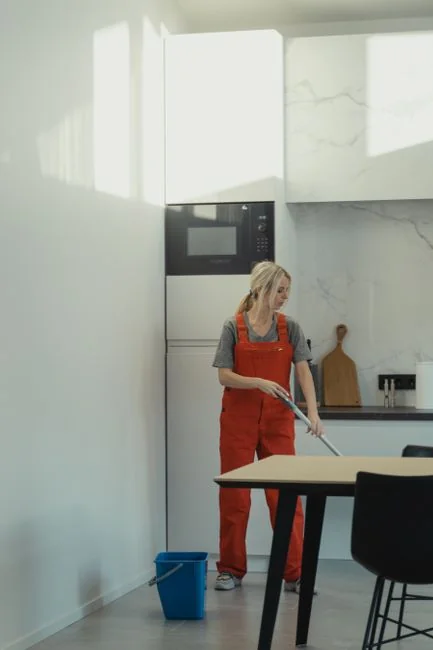 Black and white portrait of a housekeeper with cleaning supplies in a modern kitchen.